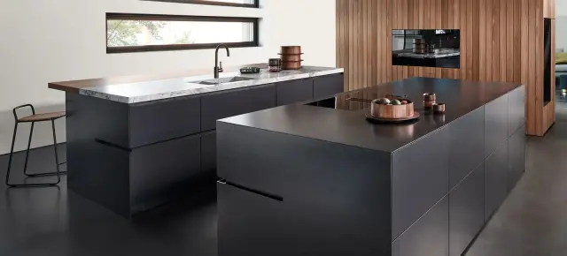 Eggersmann UNIQUE Küche mit Kochinseln aus Schwarzstahl, Hochschrank in Black Walnut und Arbeitsplatte aus Quarzit Bianco Nuvola